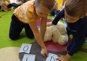 chłopcy wskazują palcami literę D na dywanie